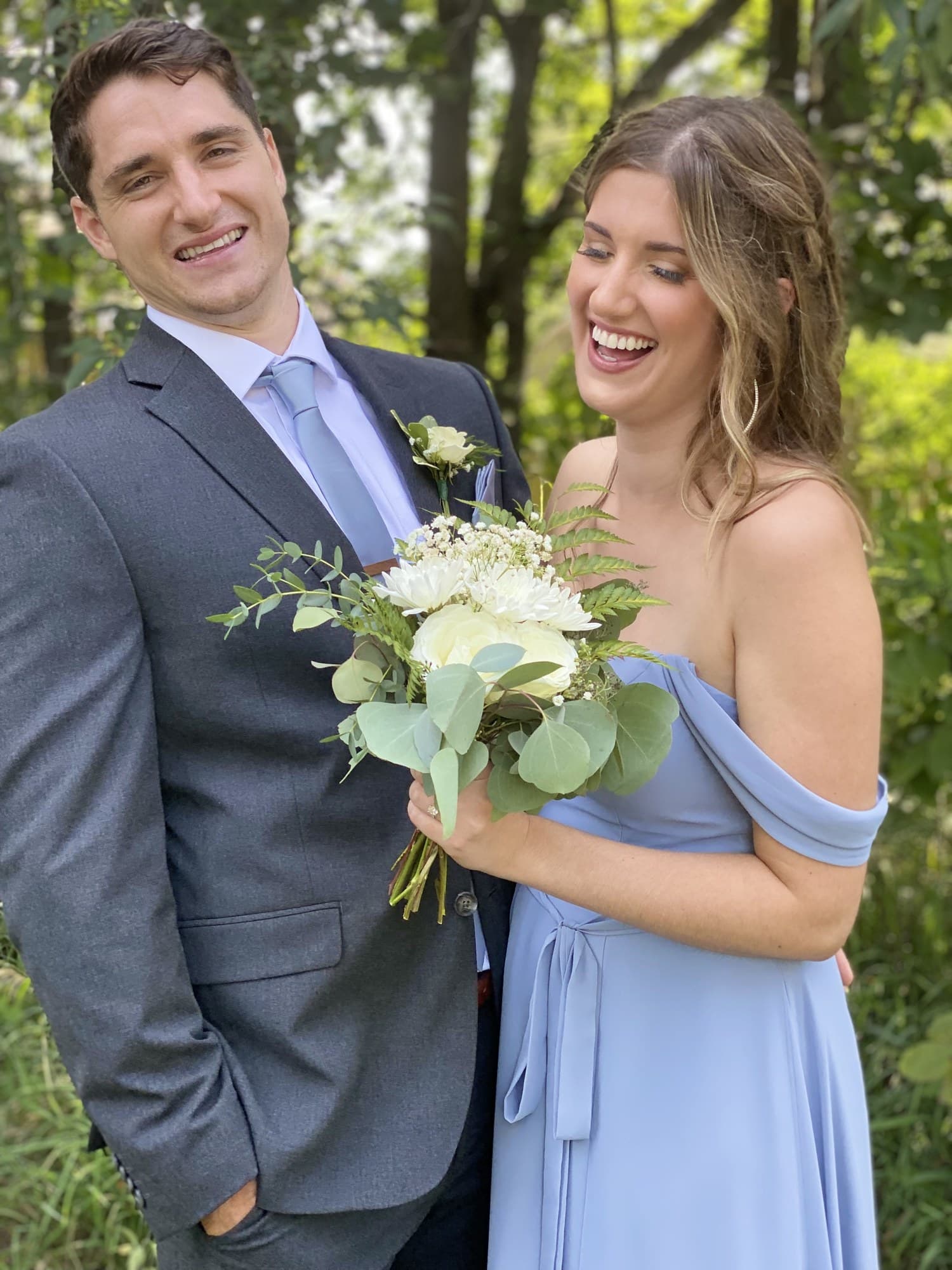 Joyful couple laughing together outdoors, white bouquet in hand