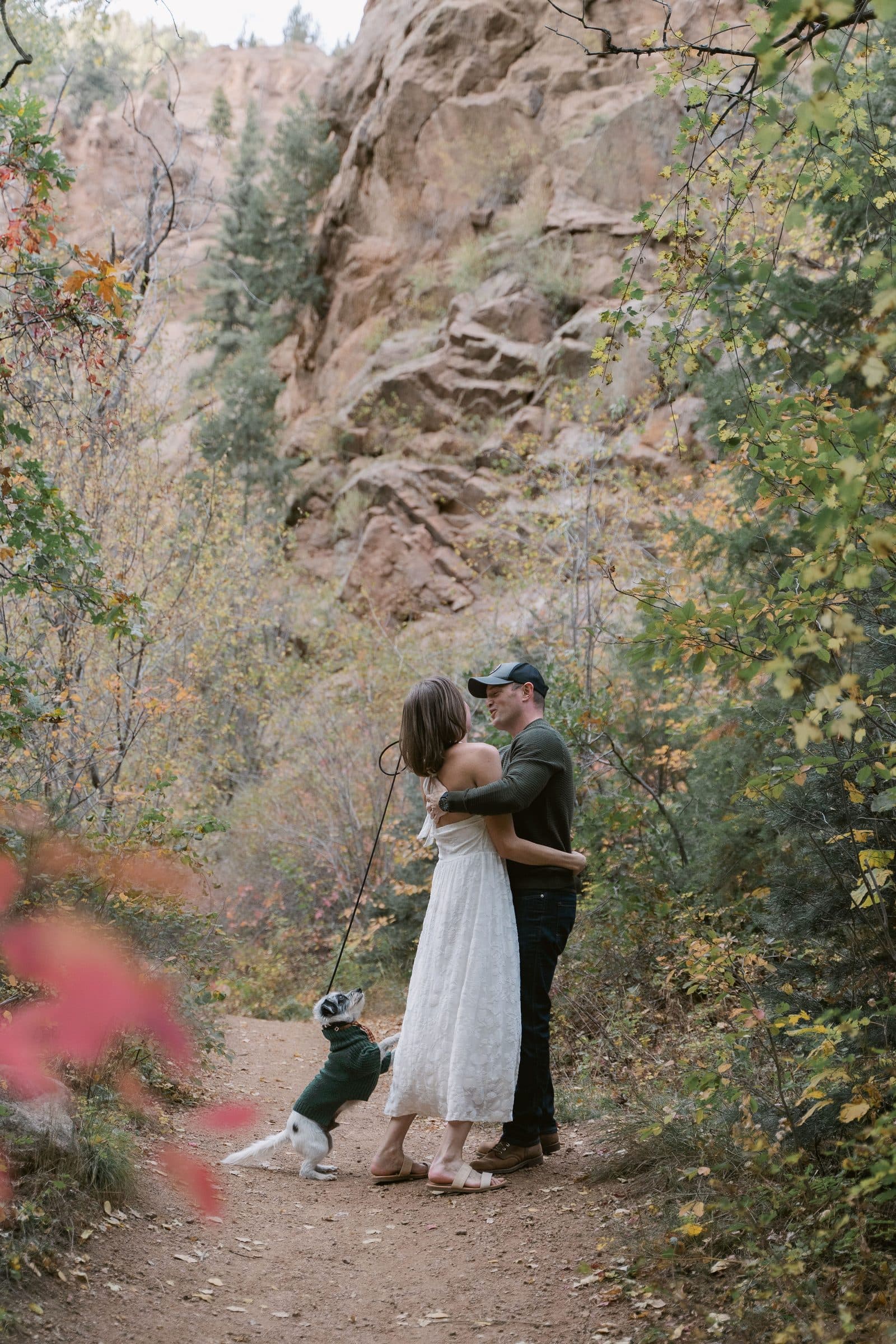 Couple embracing on a canyon trail with their dog at their feet