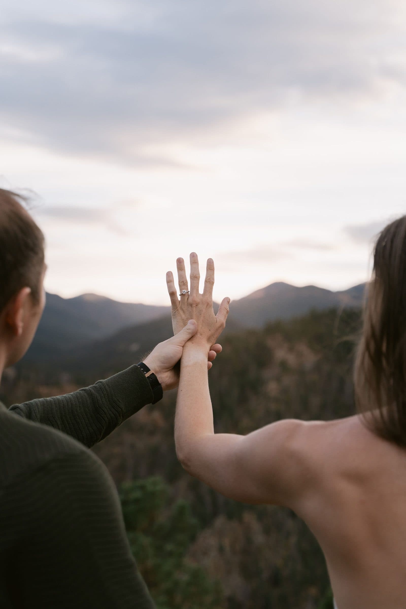 Couple pressing their palms together against a mountain sunset sky