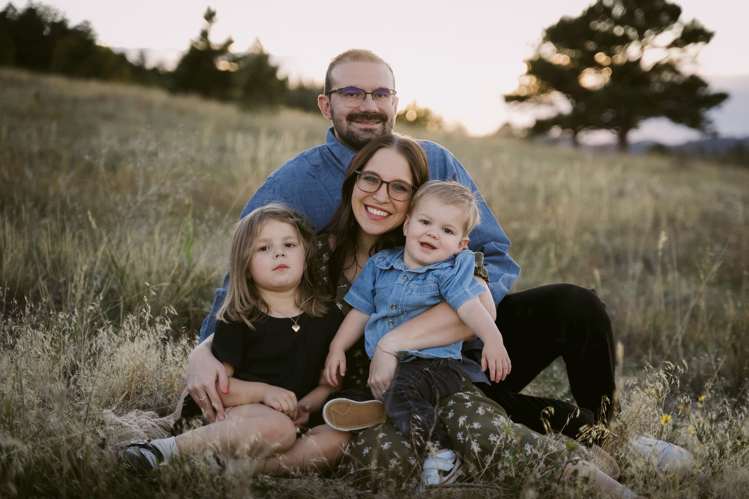 Family of four sitting together in tall grass at sunset