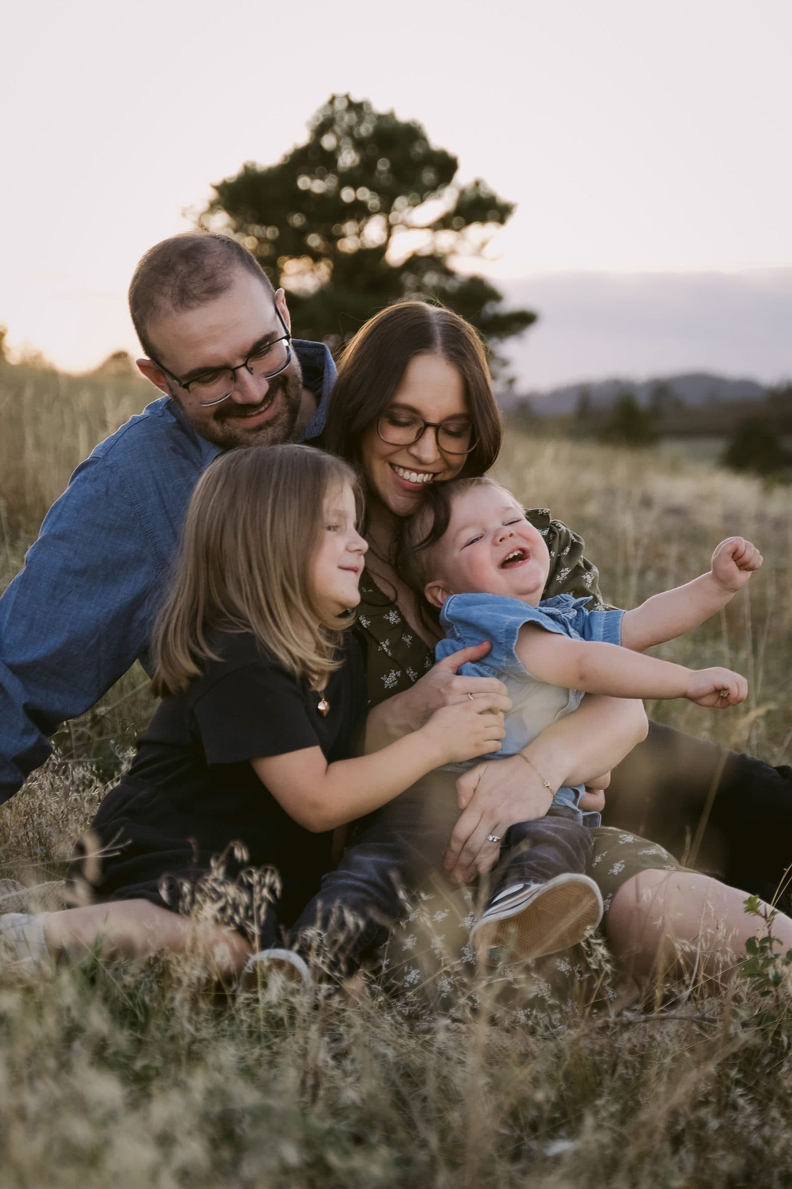 Parents snuggling their daughter and toddler son in the grass