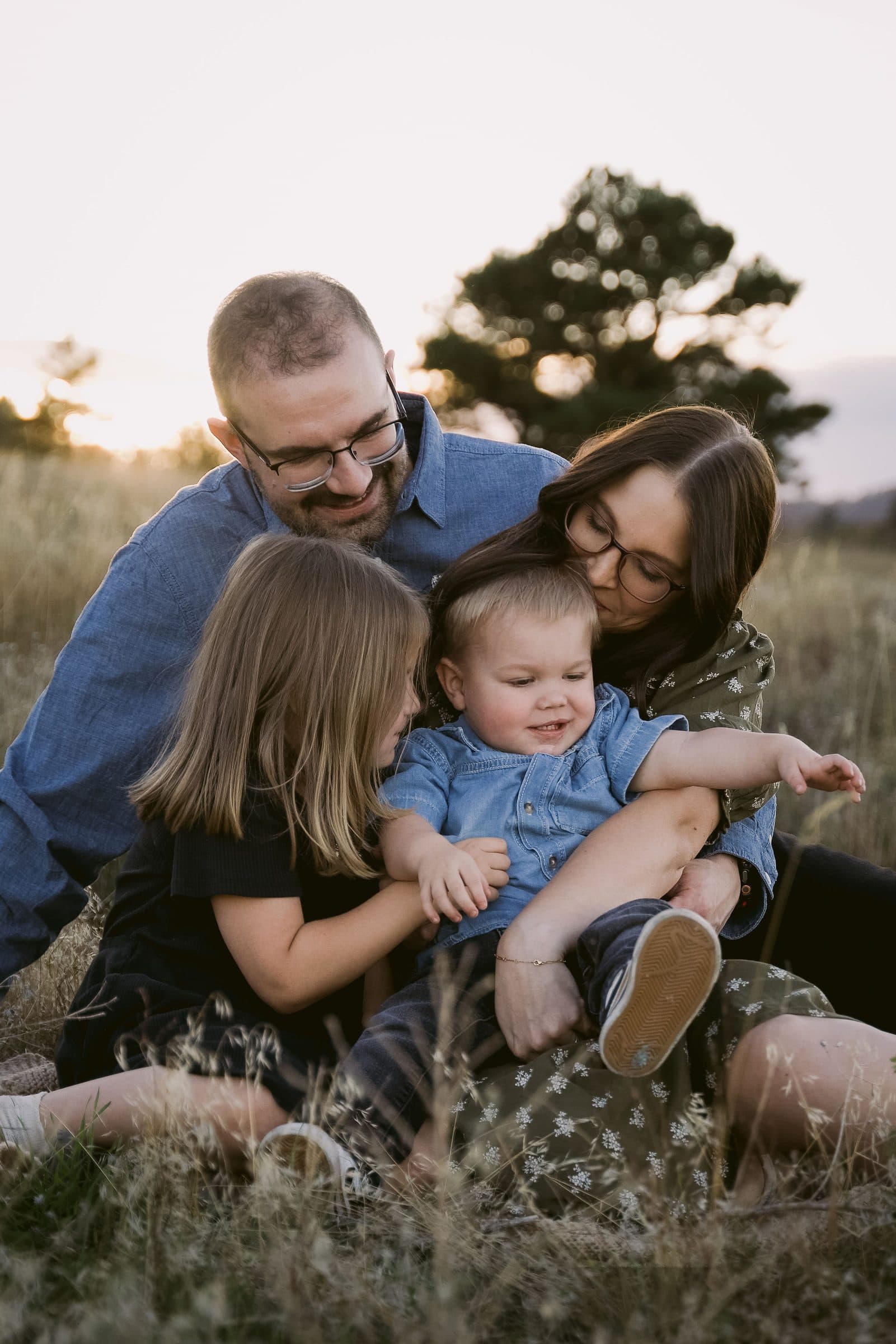 Family cuddled close in the grass, kids laughing on their parents' laps