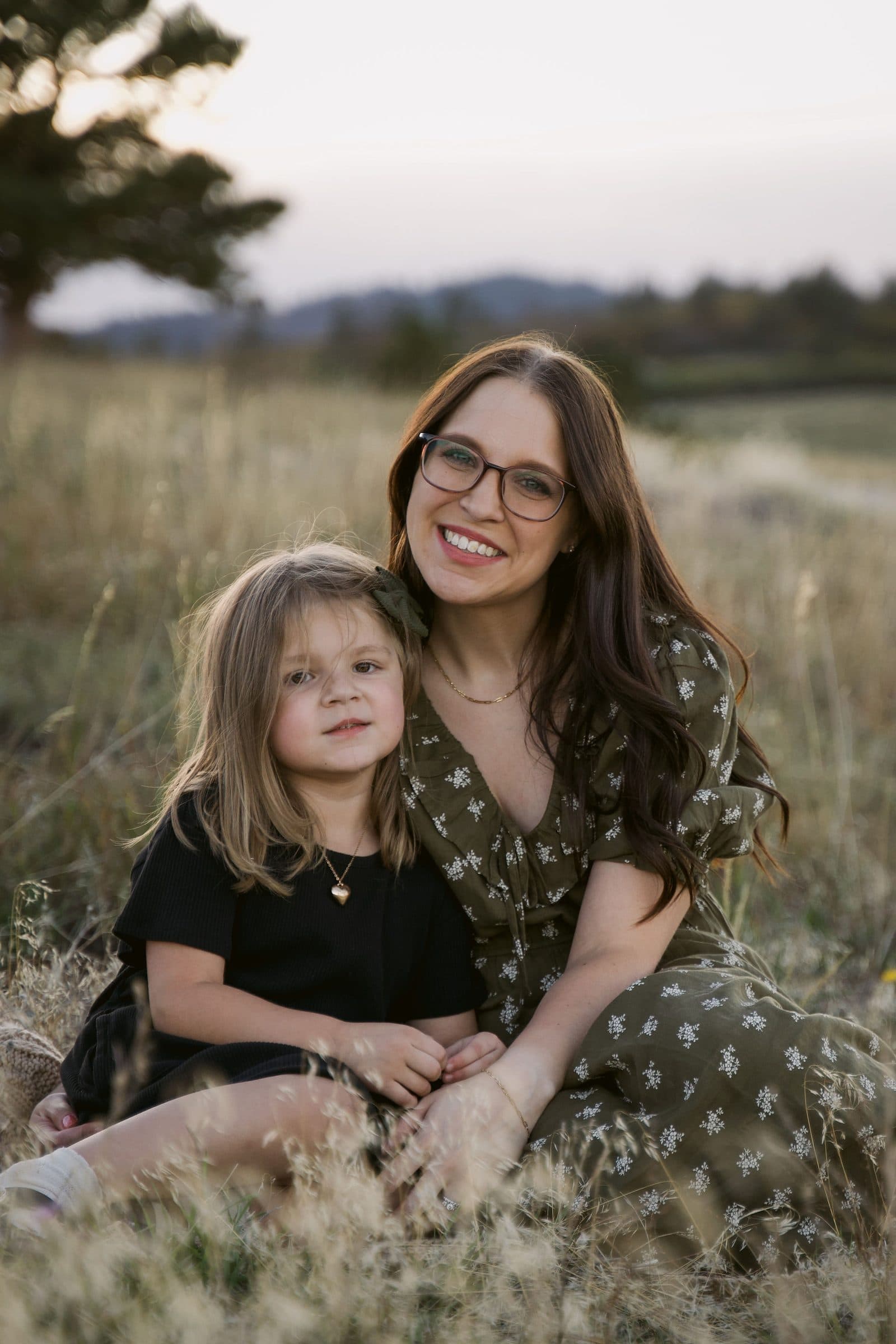 Mother hugging her daughter in the tall grass at golden hour