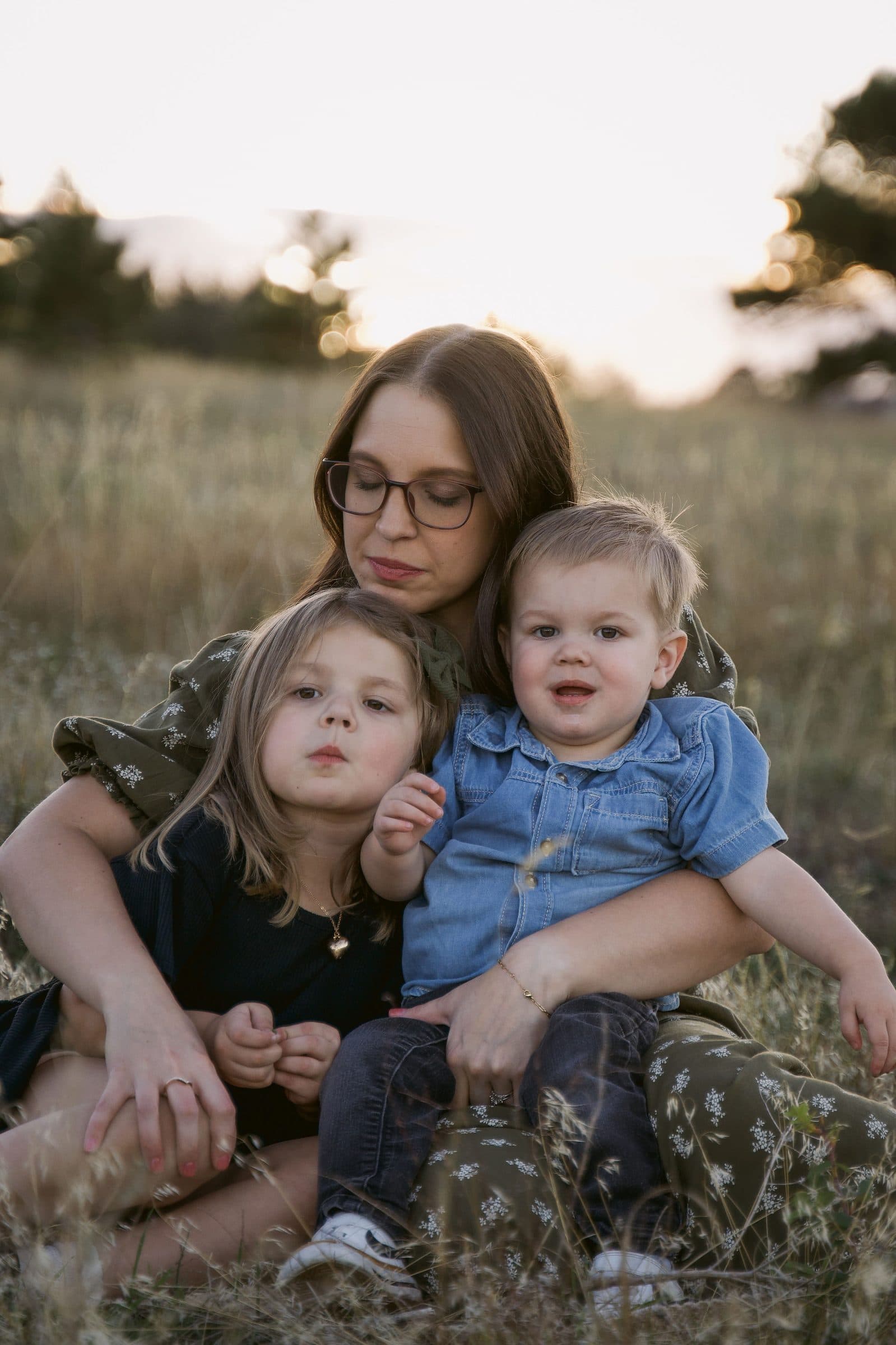 Mother holding her daughter and toddler son close in the grass