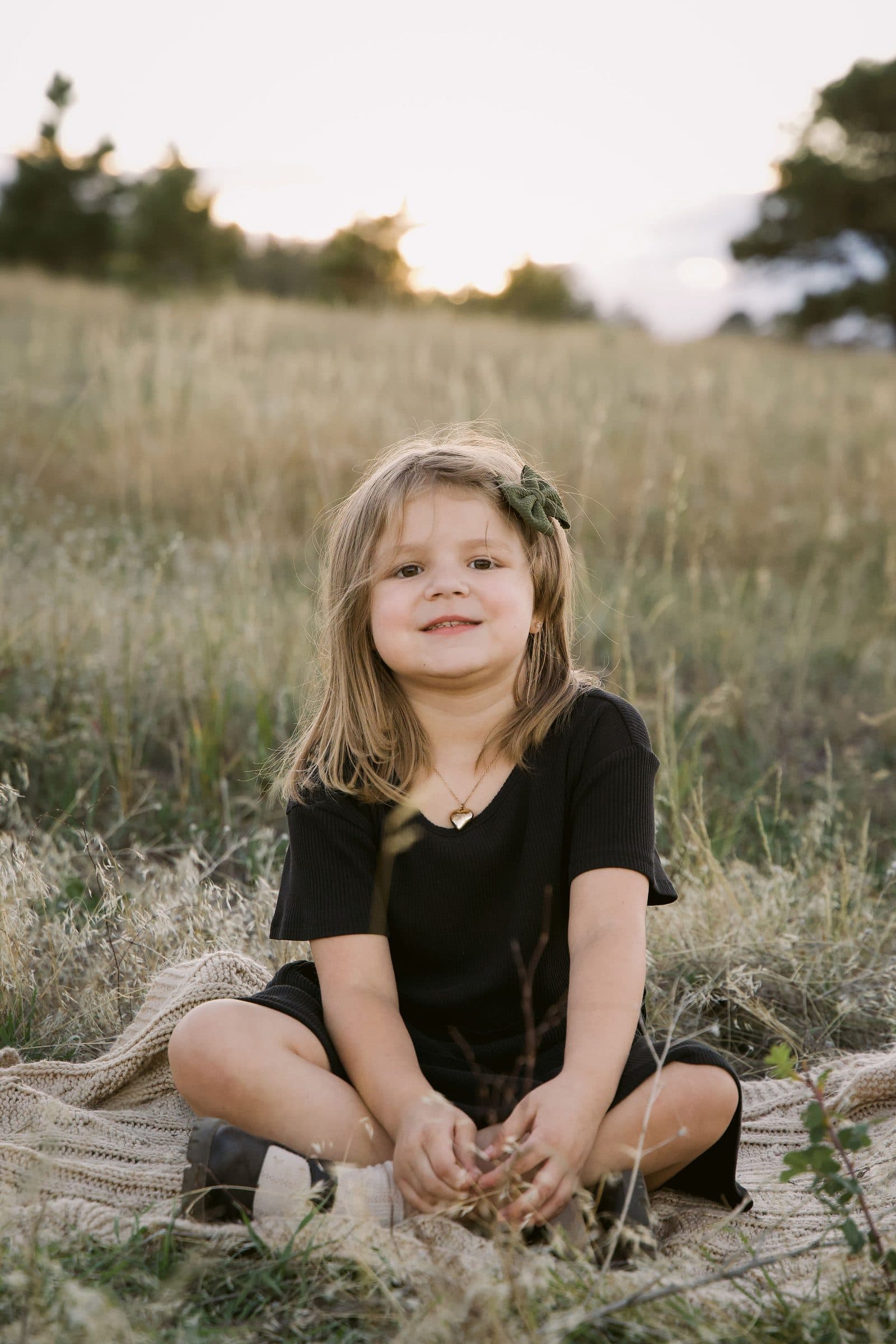 Little girl in a black dress sitting cross-legged in the grass, smiling