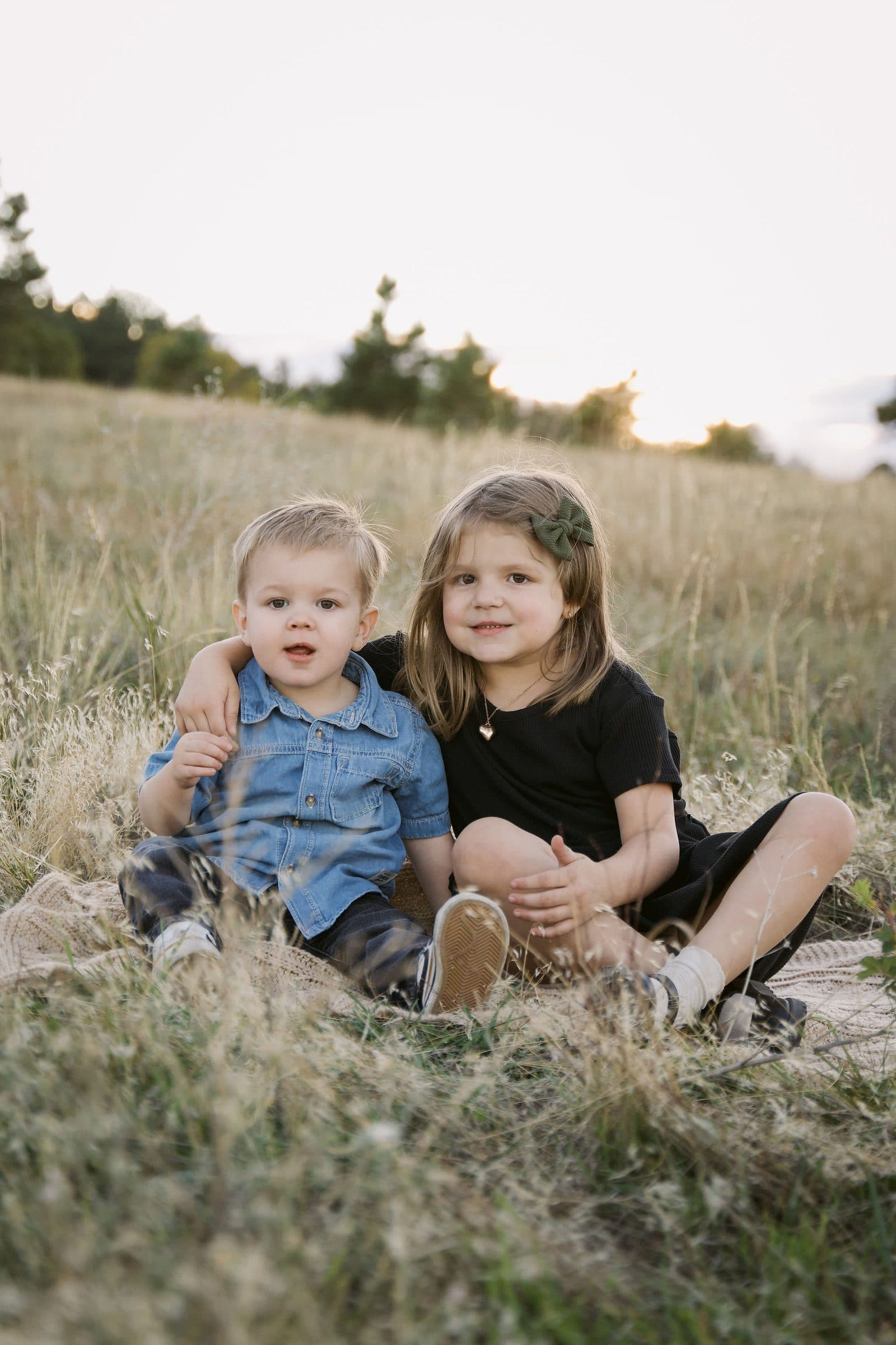 Big sister and little brother sitting together on a blanket in the grass