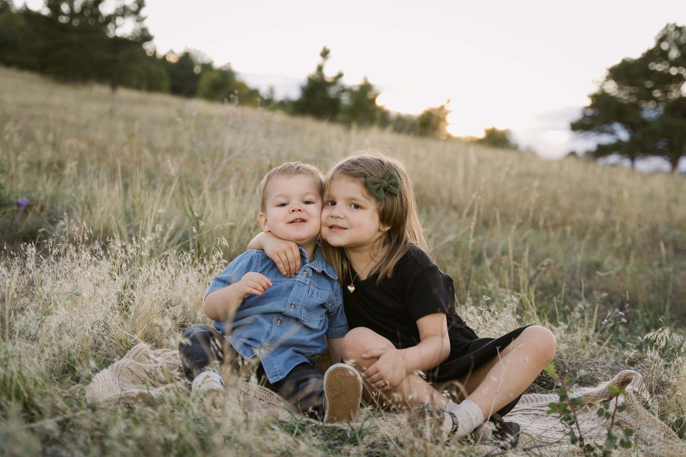 Siblings leaning into each other in a grassy field at sunset