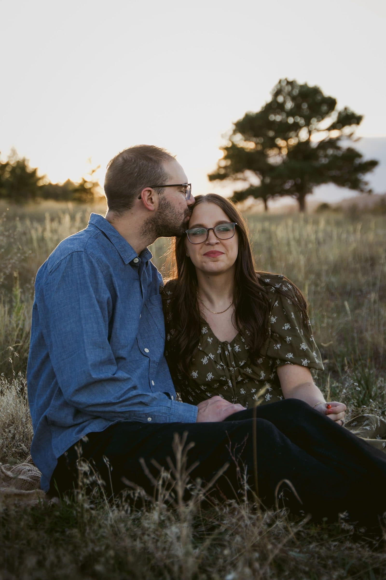 Father kissing mother's forehead as they sit in the grass
