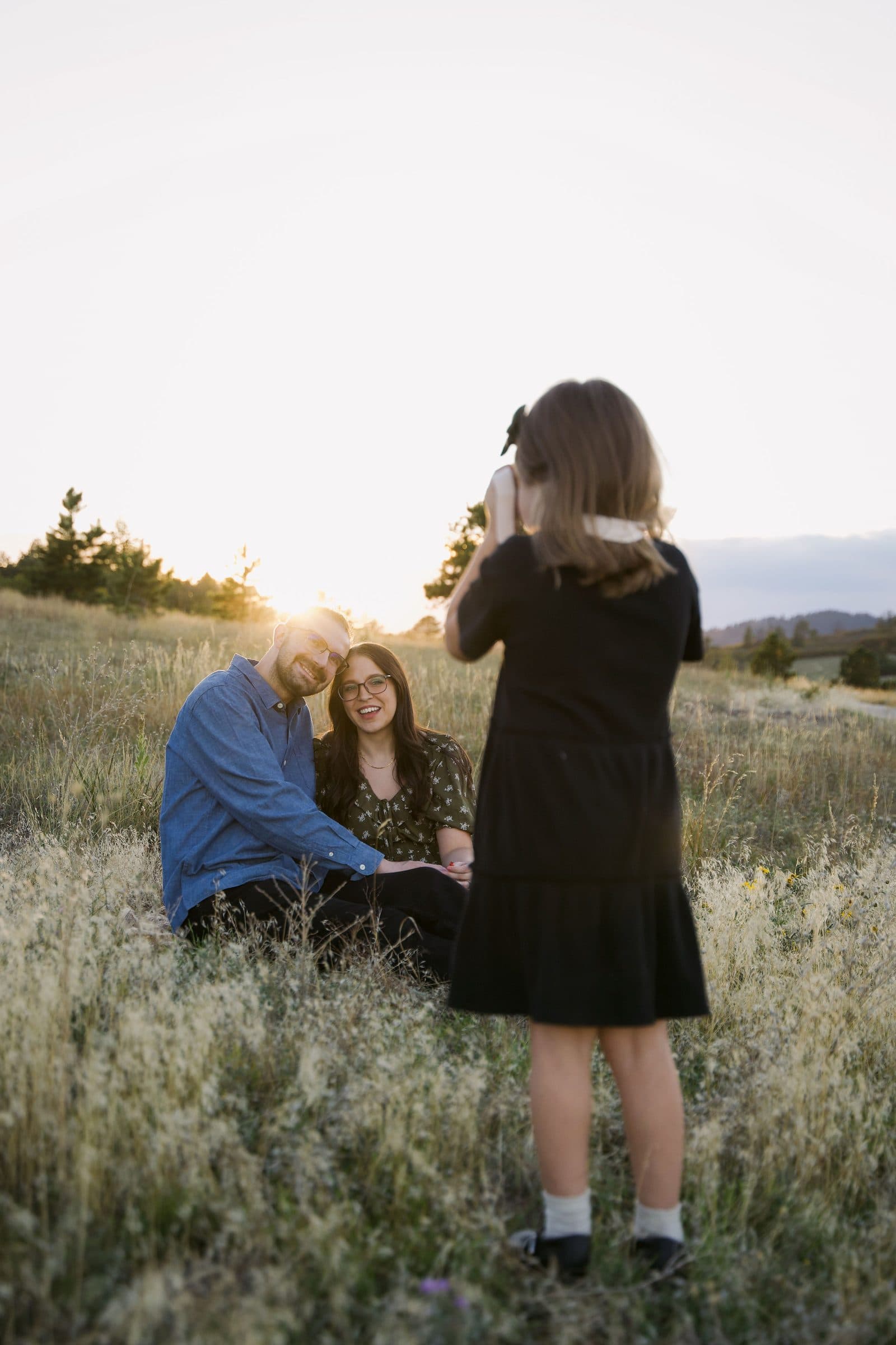 Little girl taking a photo of her parents in the grass at sunset