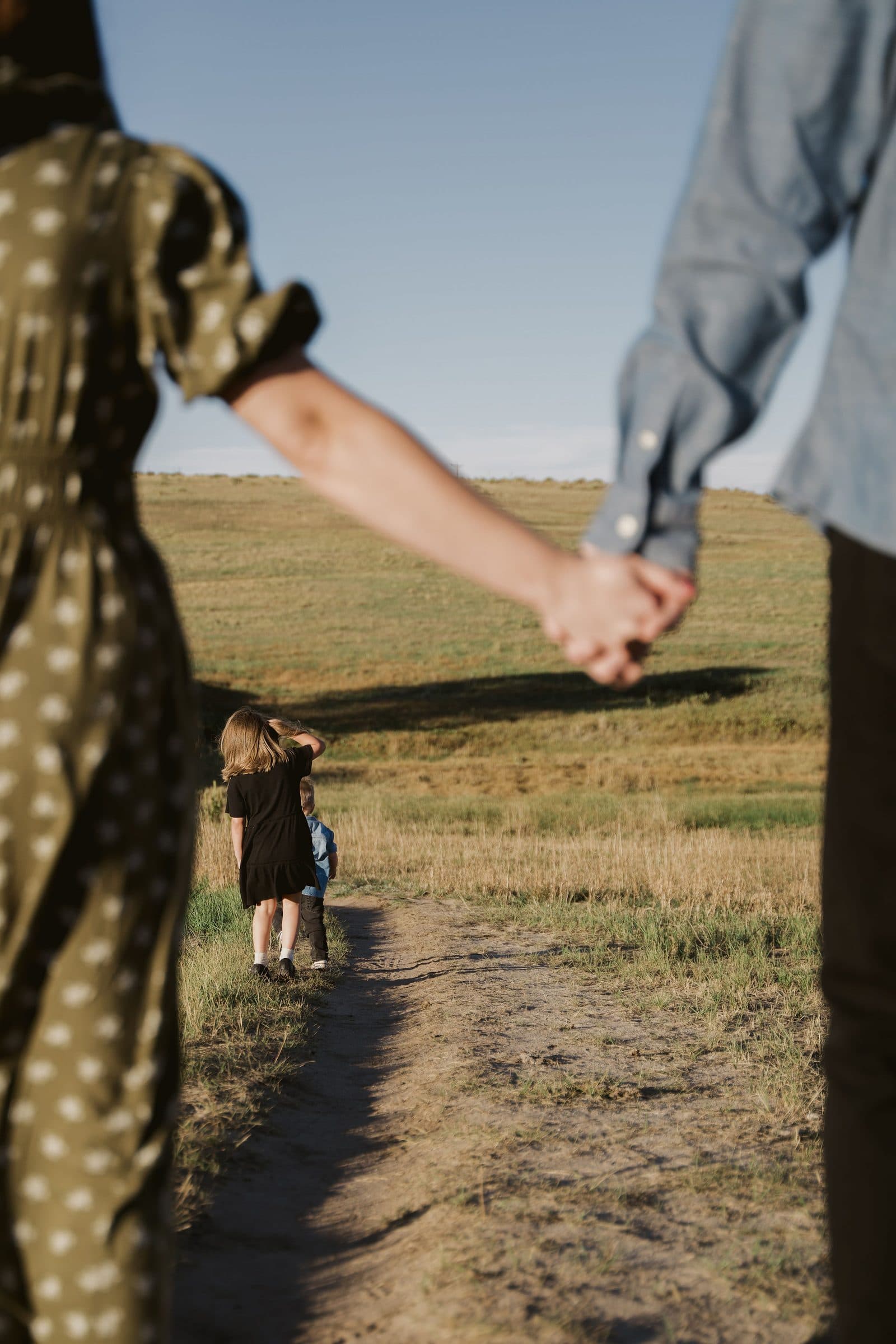 Parents holding hands on a dirt path as their kids run ahead