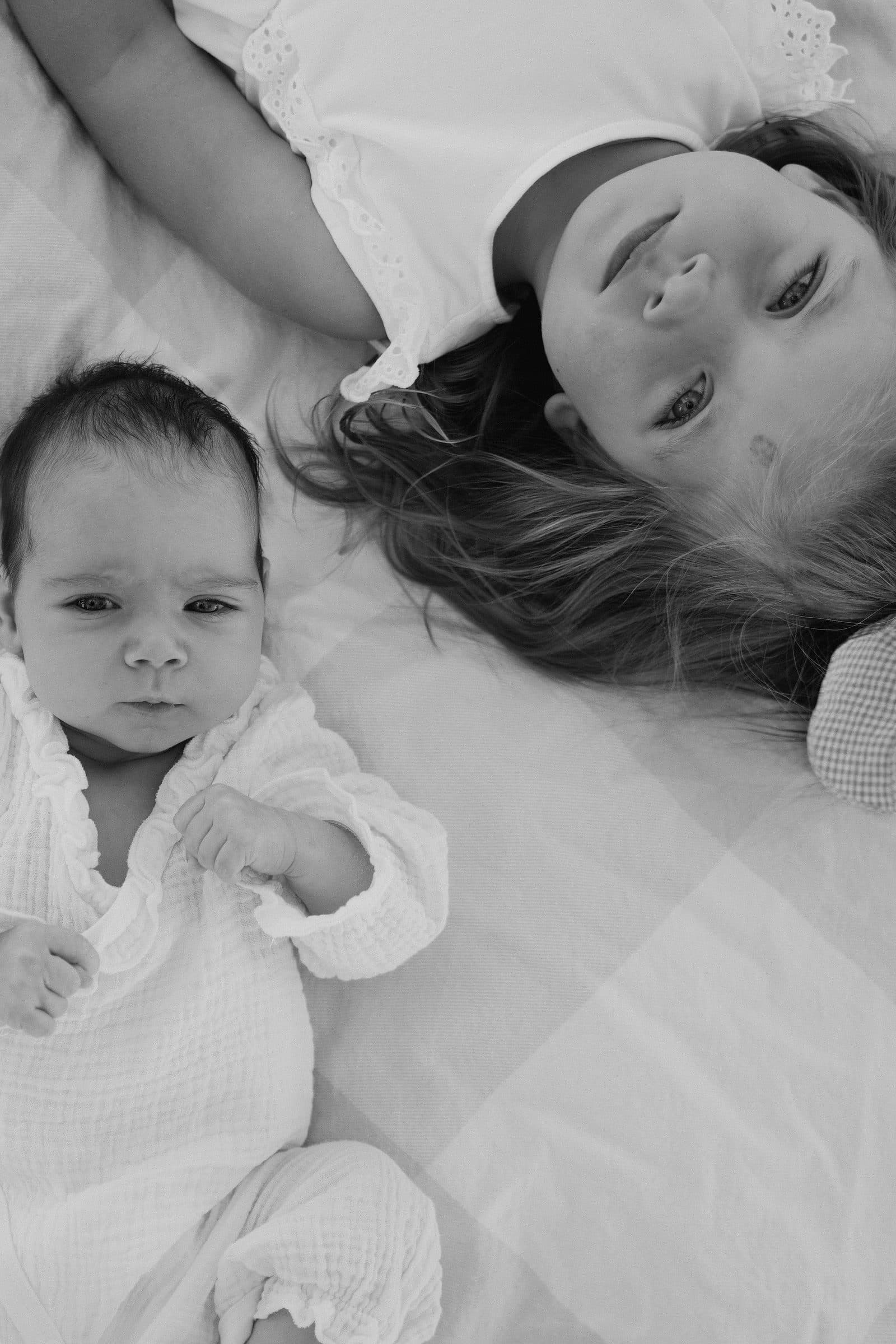 Black and white of a newborn lying beside an older child on a blanket