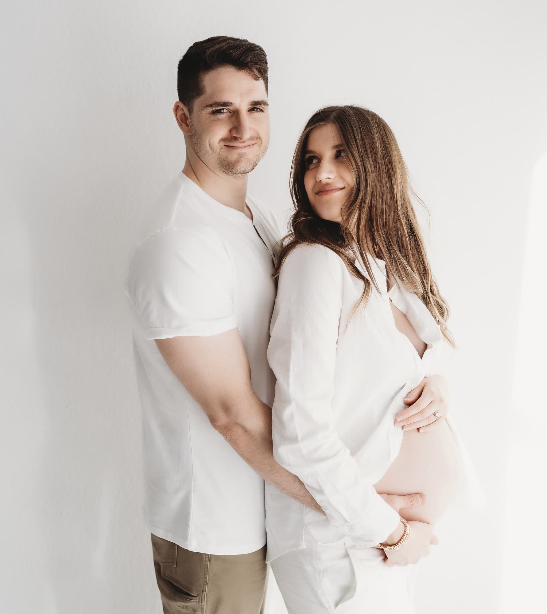 Maternity portrait in a bright white studio, partner holding the belly
