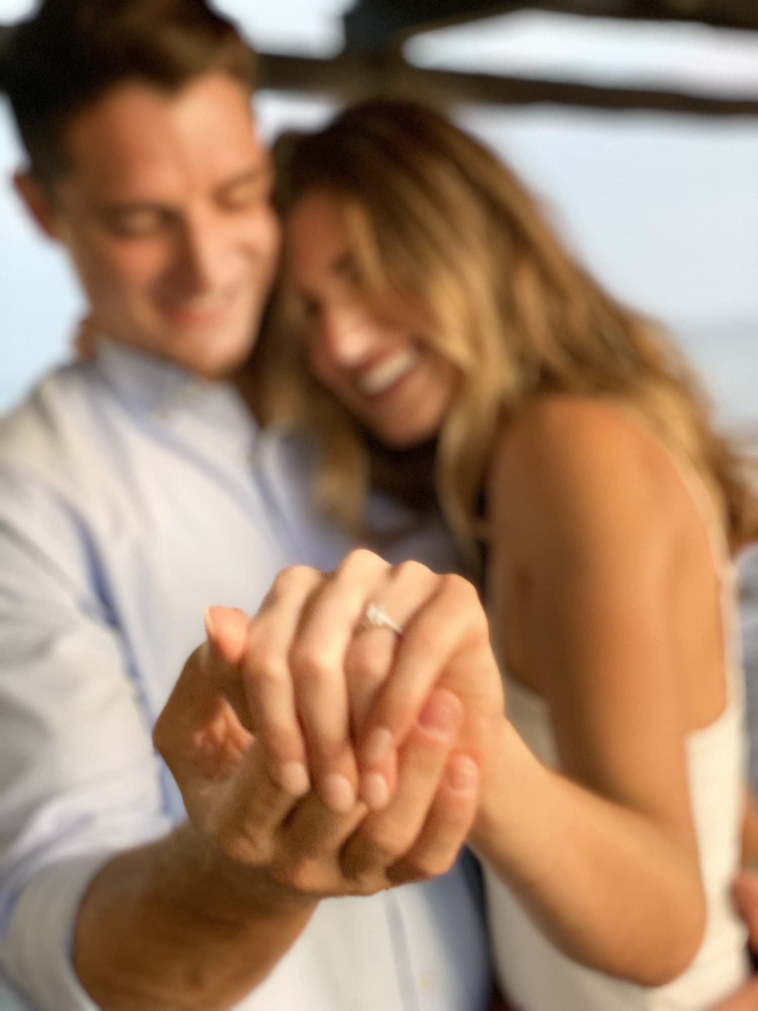 Close-up of an engagement ring with a couple embracing in soft focus
