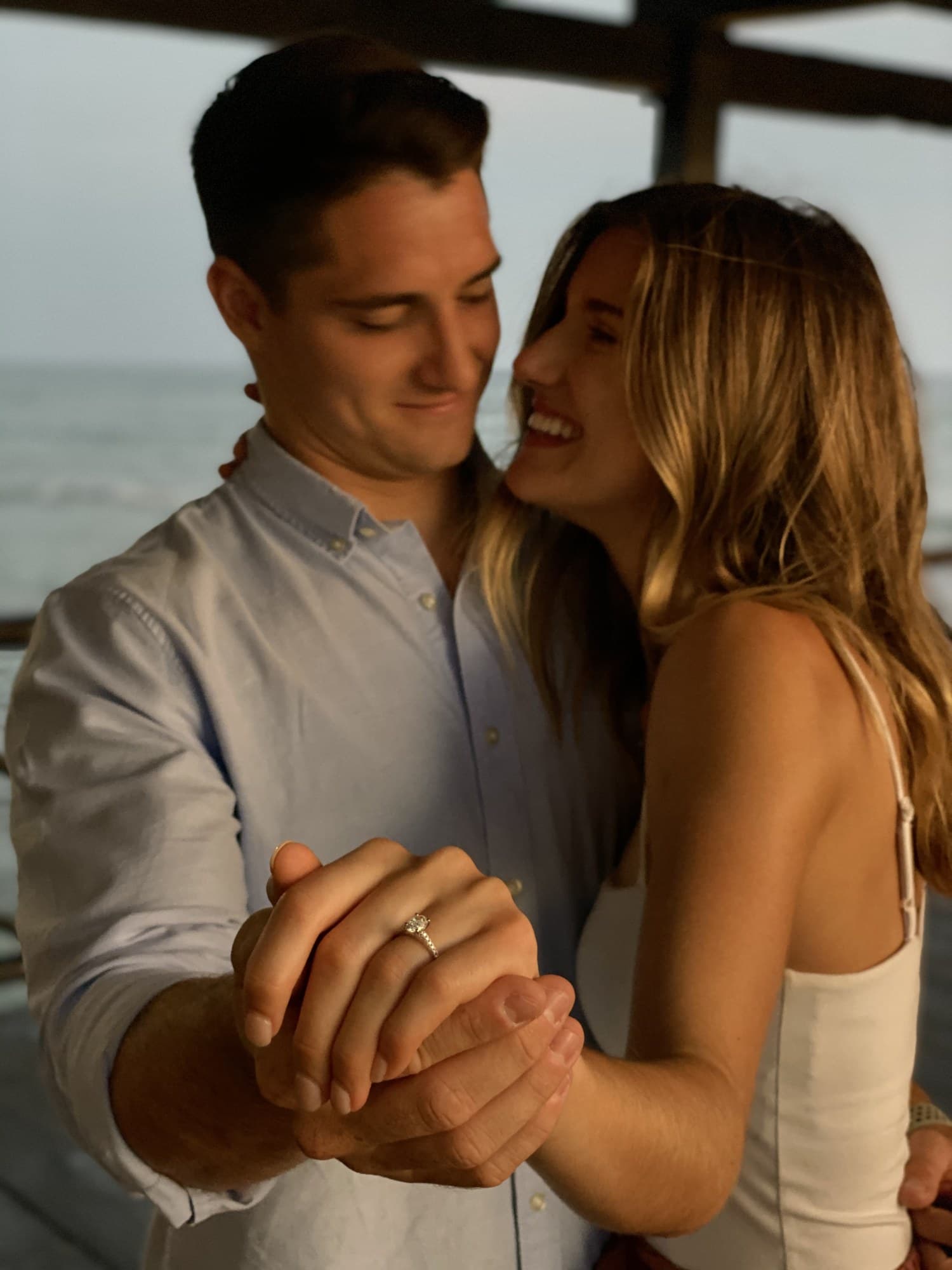 Engaged couple smiling on a balcony at dusk, ring in the foreground