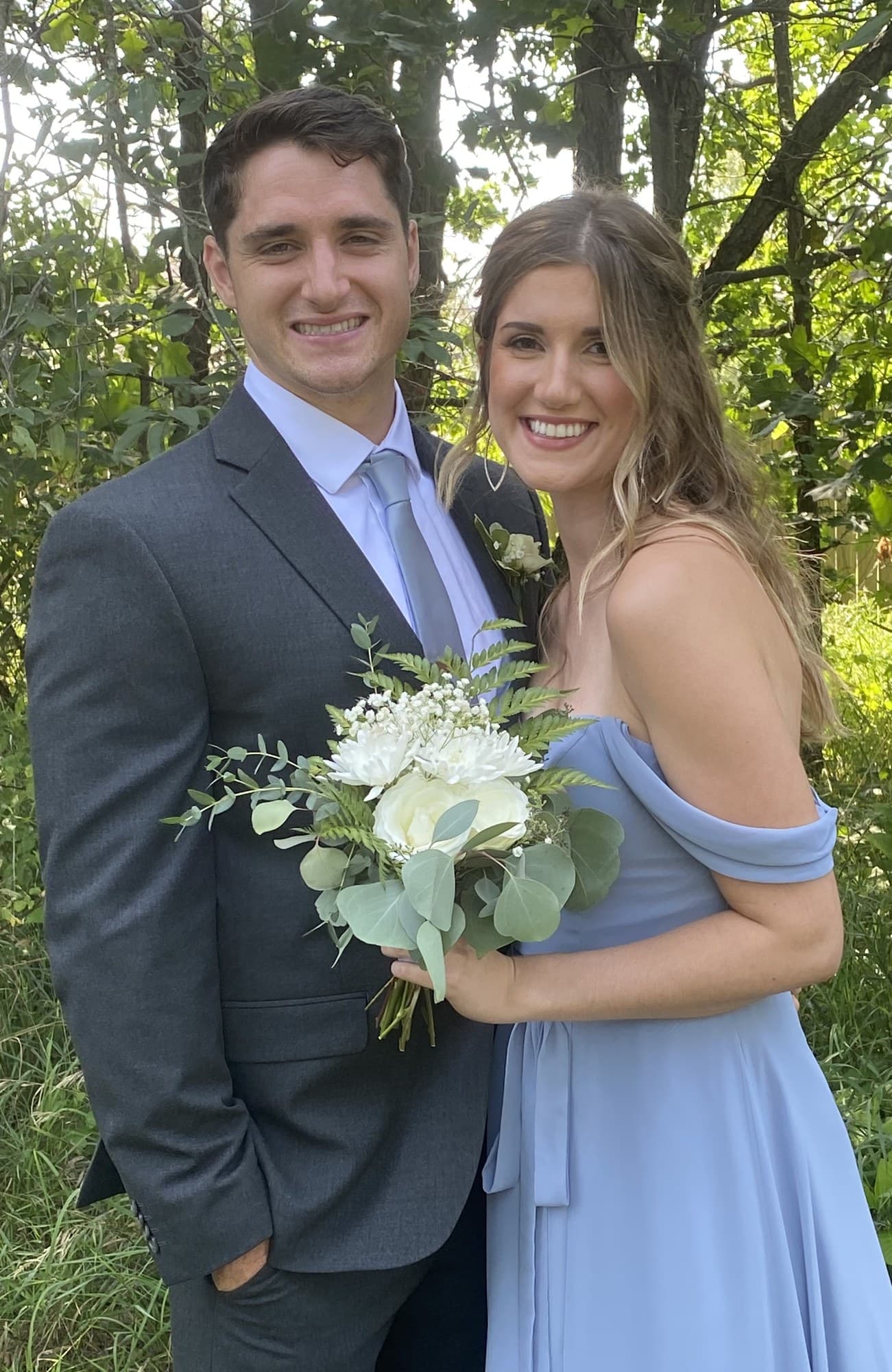 Couple in formal attire posing outdoors with a white bouquet