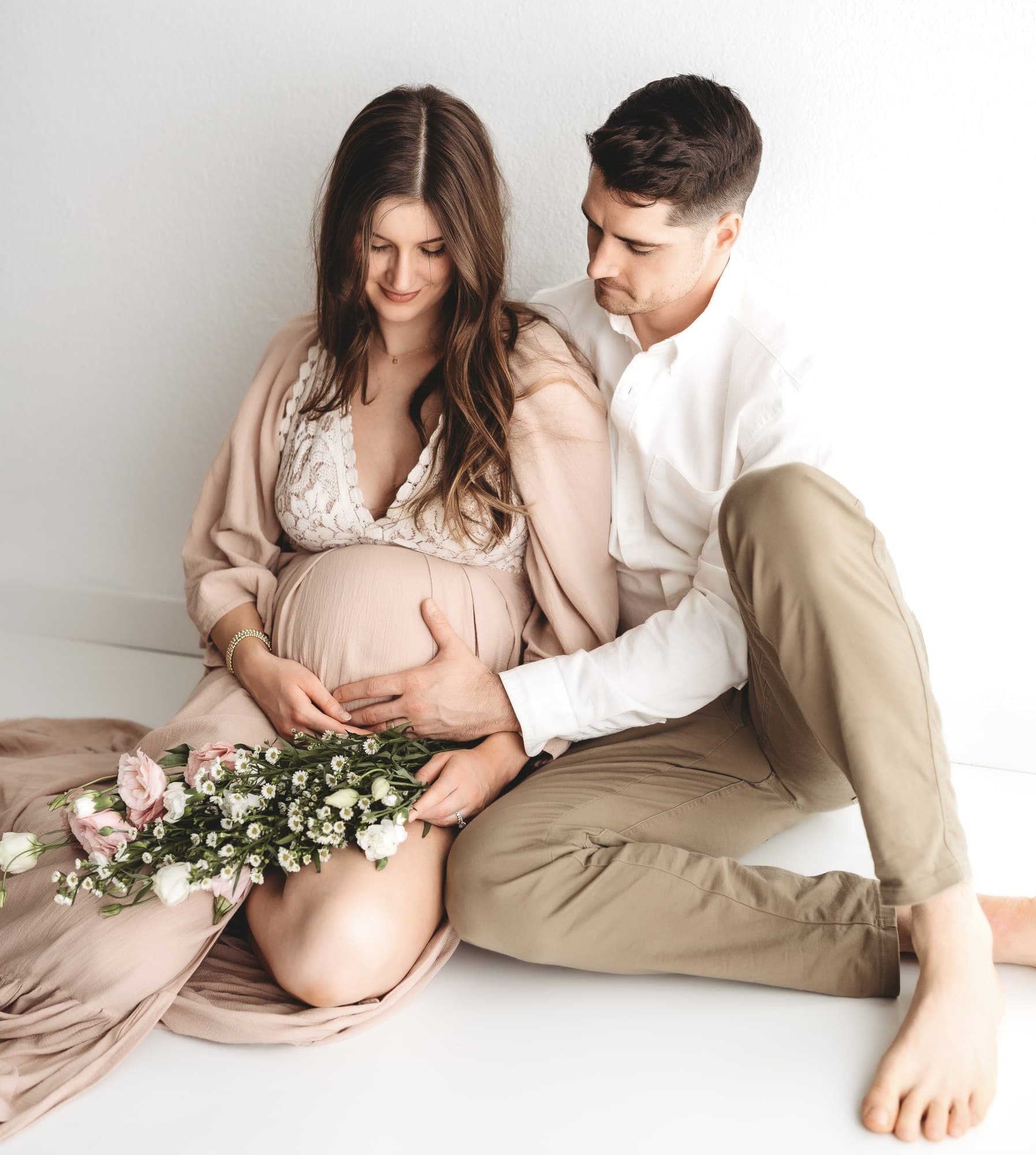 Seated maternity portrait with wildflowers in a white studio